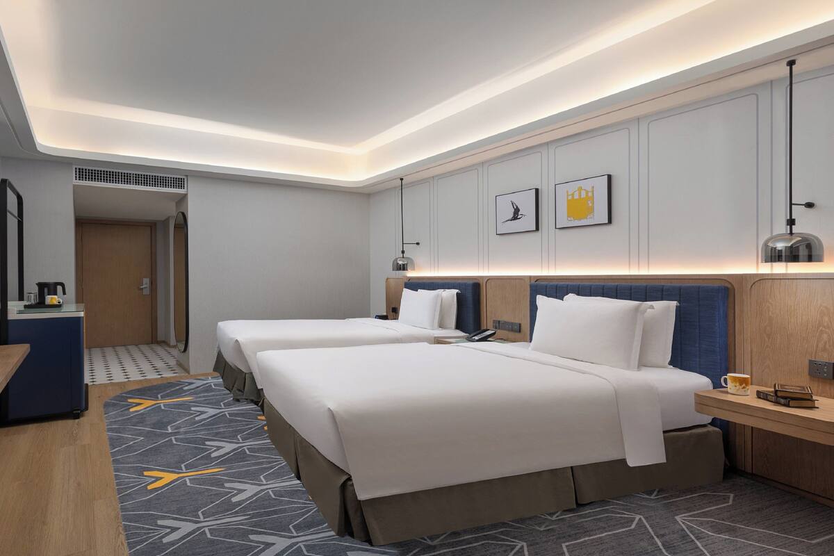 A hotel room with two beds, a desk, a mirror, and a TV.