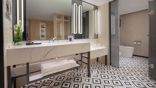 Un baño moderno con tocador de mármol, un espejo grande con luces verticales, piso estampado y cabina de ducha de vidrio.