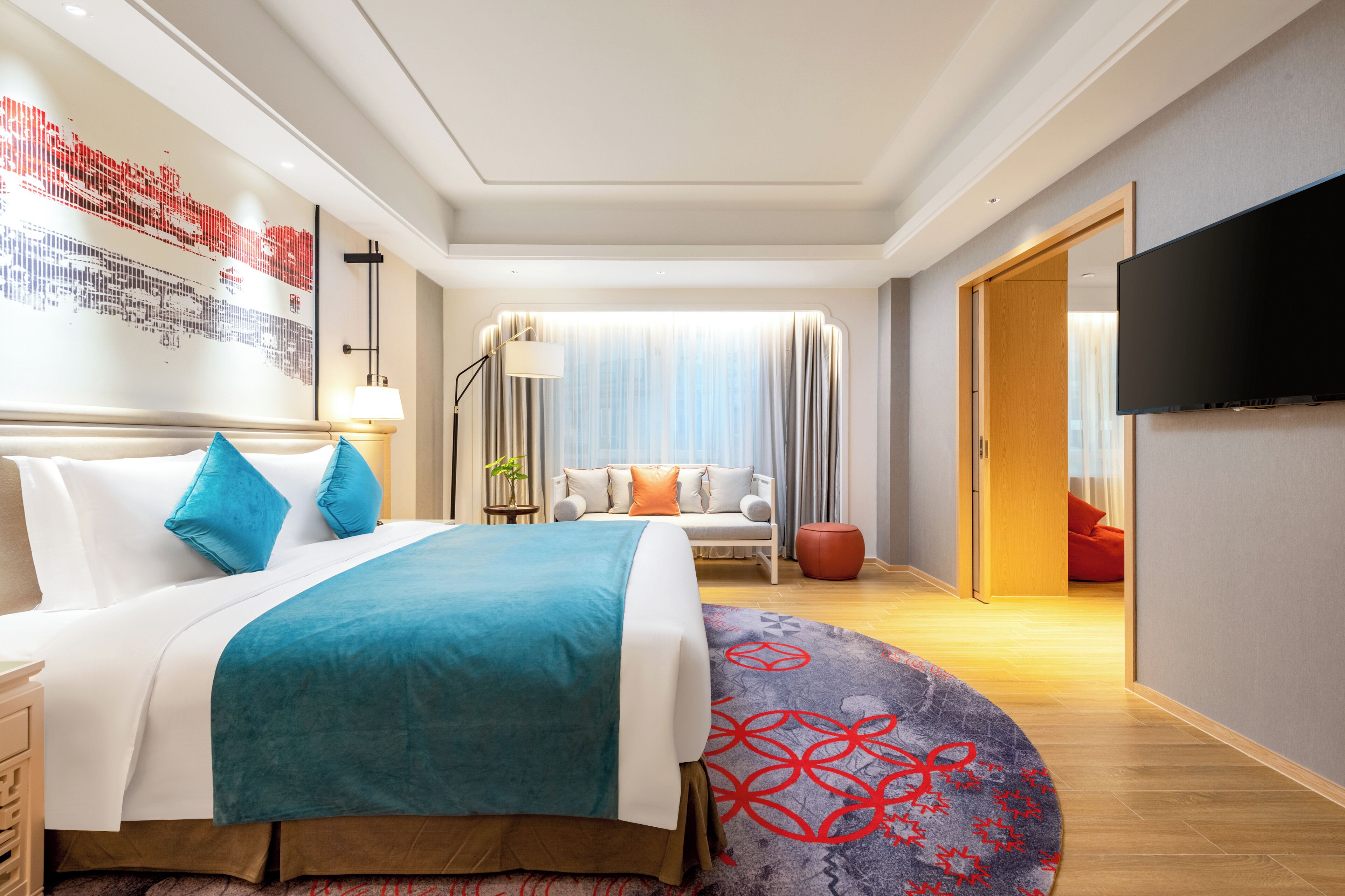 A modern hotel room with a large bed, a flat-screen TV, a sofa, and a dining area.