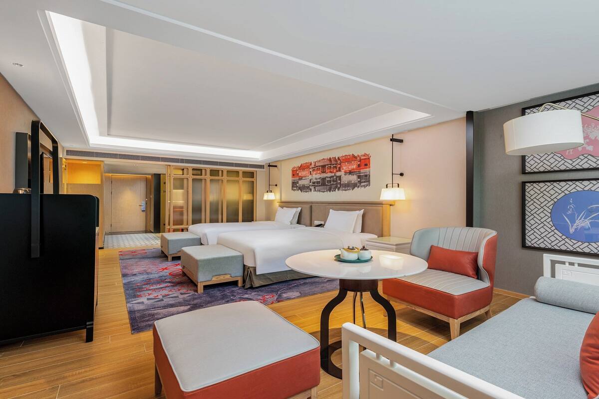 A hotel room with a bed, two bedside tables, a sofa, a small table, and a decorative wall.