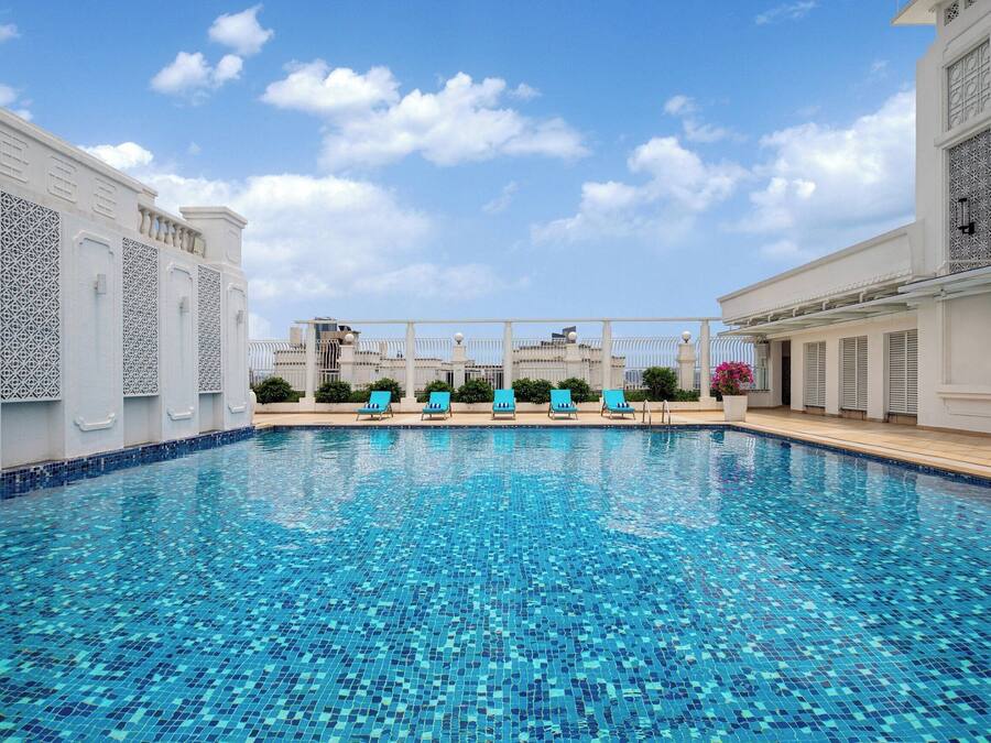 Una piscina con piso azul de azulejos y paredes blancas, rodeada de sillones de descanso y una pérgola.