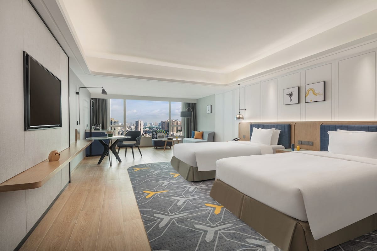 A hotel room with two beds, a desk, and a view of the city.