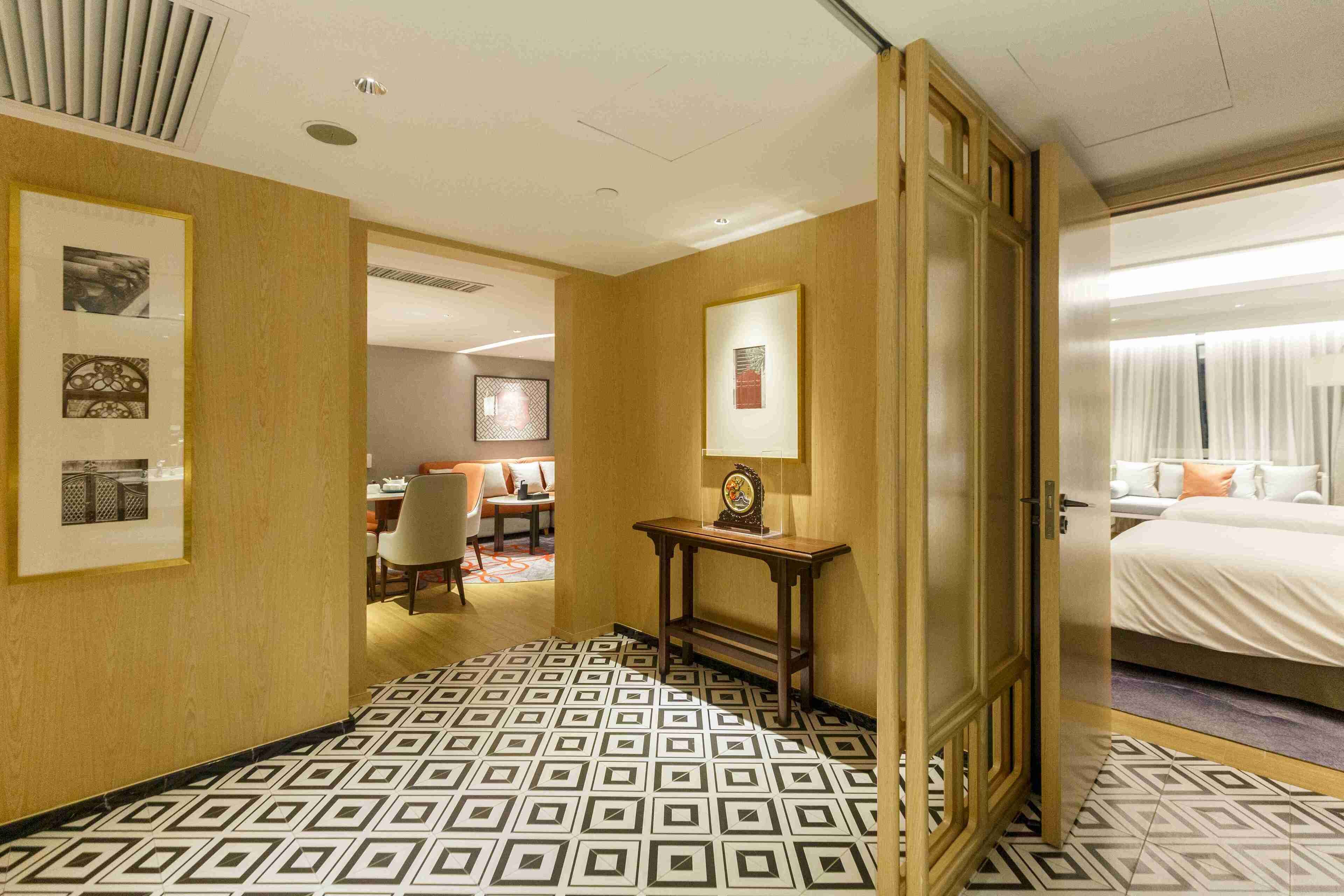 A hotel room with a patterned floor, a bed, a bedside table, and a mirror.