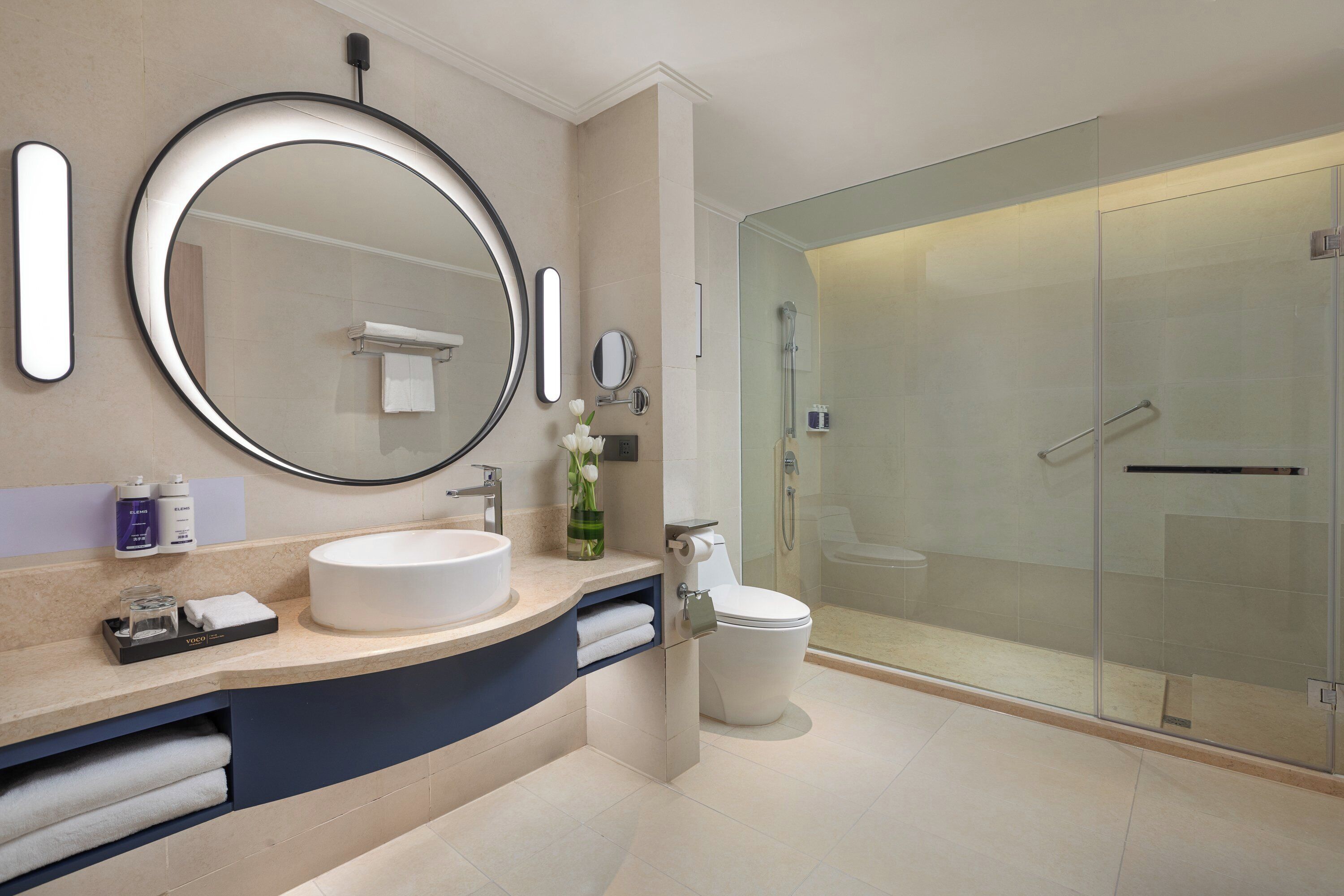 A modern bathroom with a round mirror, a sink, a toilet, and a glass-enclosed shower.