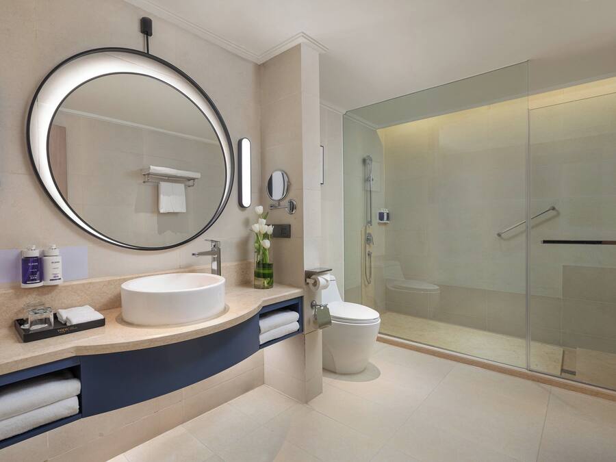 A modern bathroom with a round mirror, a sink, a toilet, and a glass-enclosed shower.
