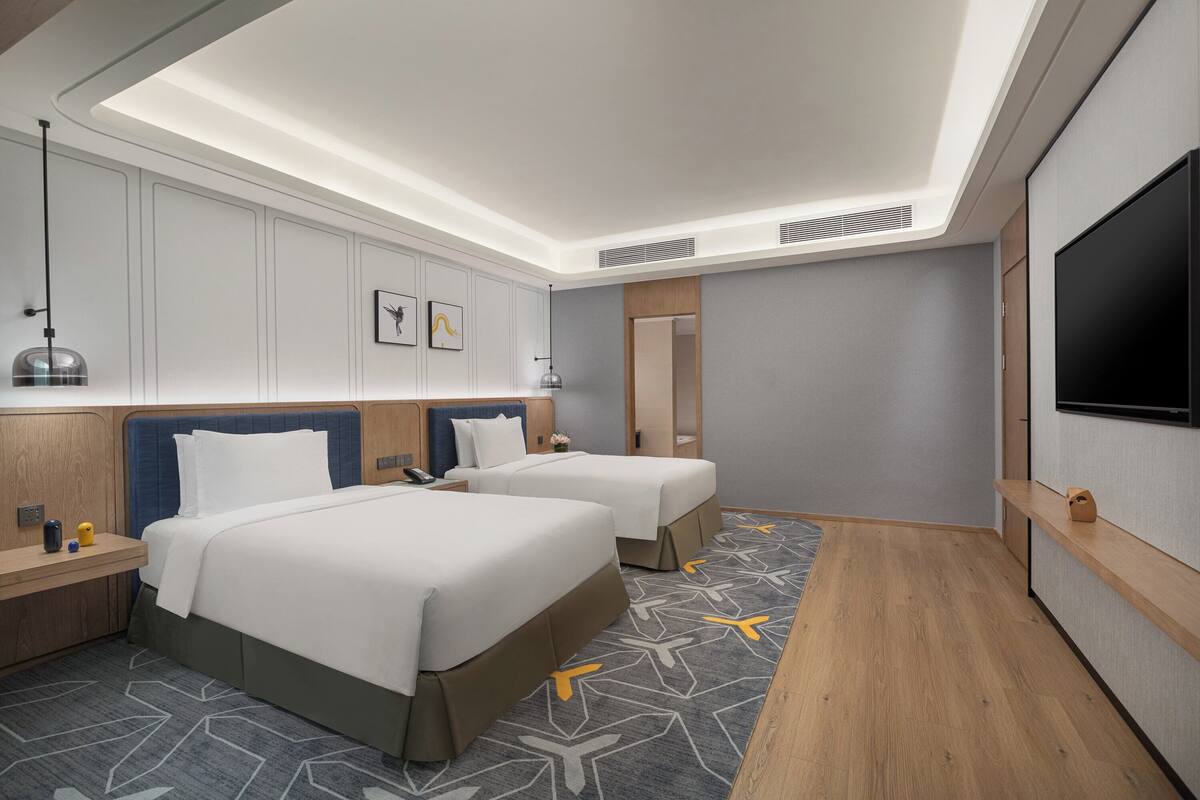 A modern hotel room with two beds, a flat-screen TV, a desk, and a large mirror.