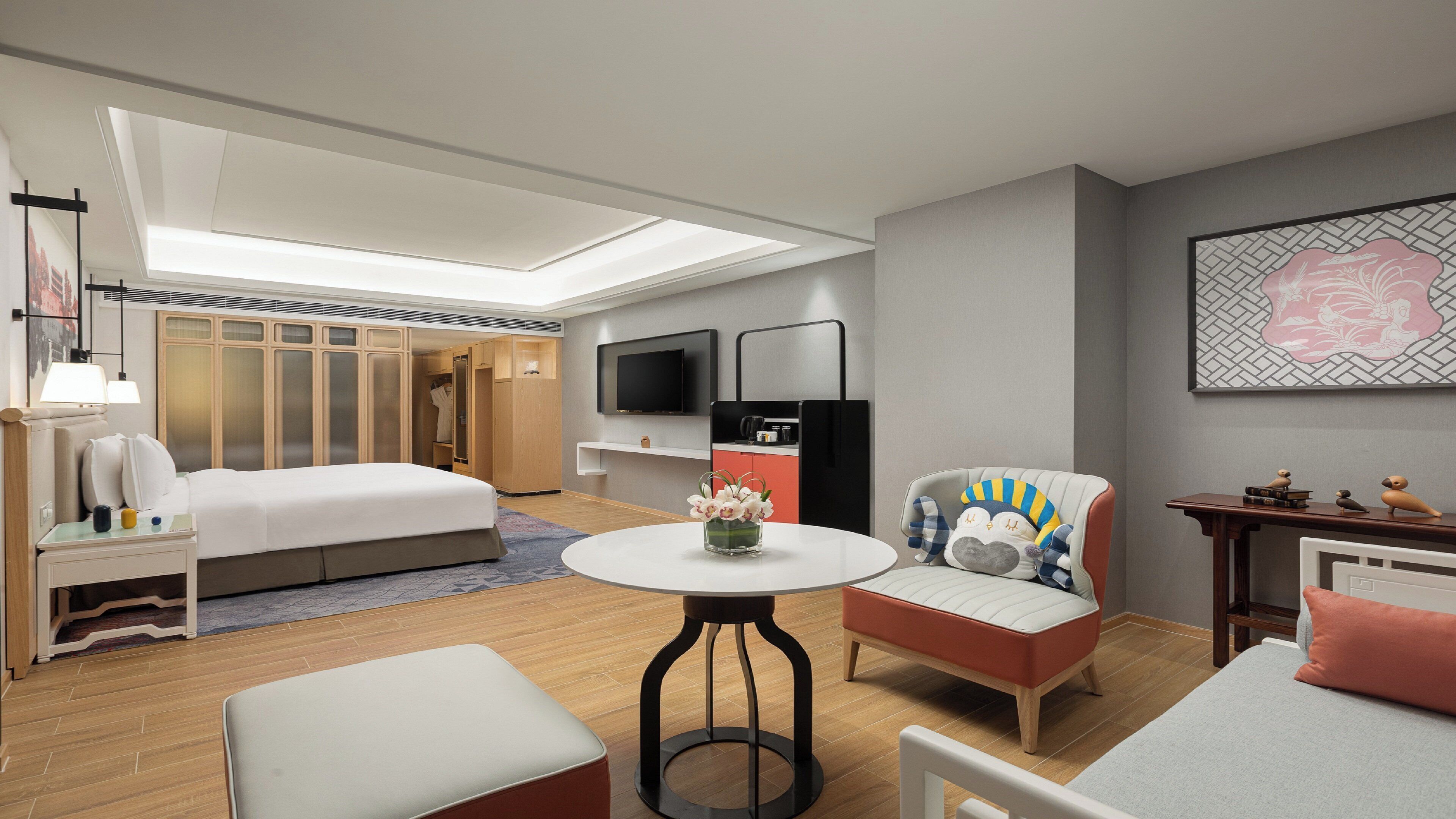 Una habitación de hotel moderna con una cama, una mesa redonda con un jarrón de flores, un televisor y un armario.