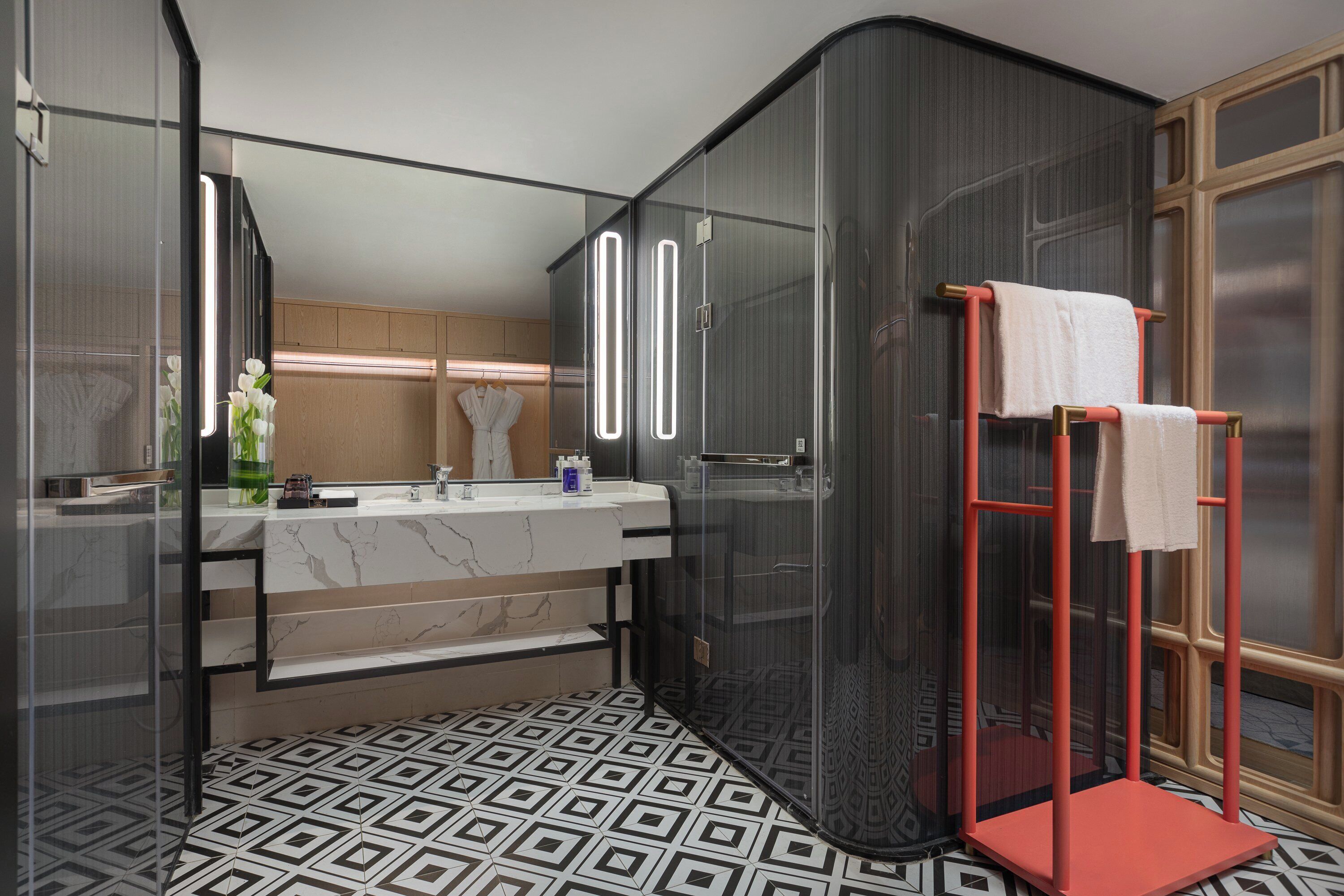 Un baño moderno con tocador de mármol, cabina de ducha de vidrio y suelo con diseño geométrico.