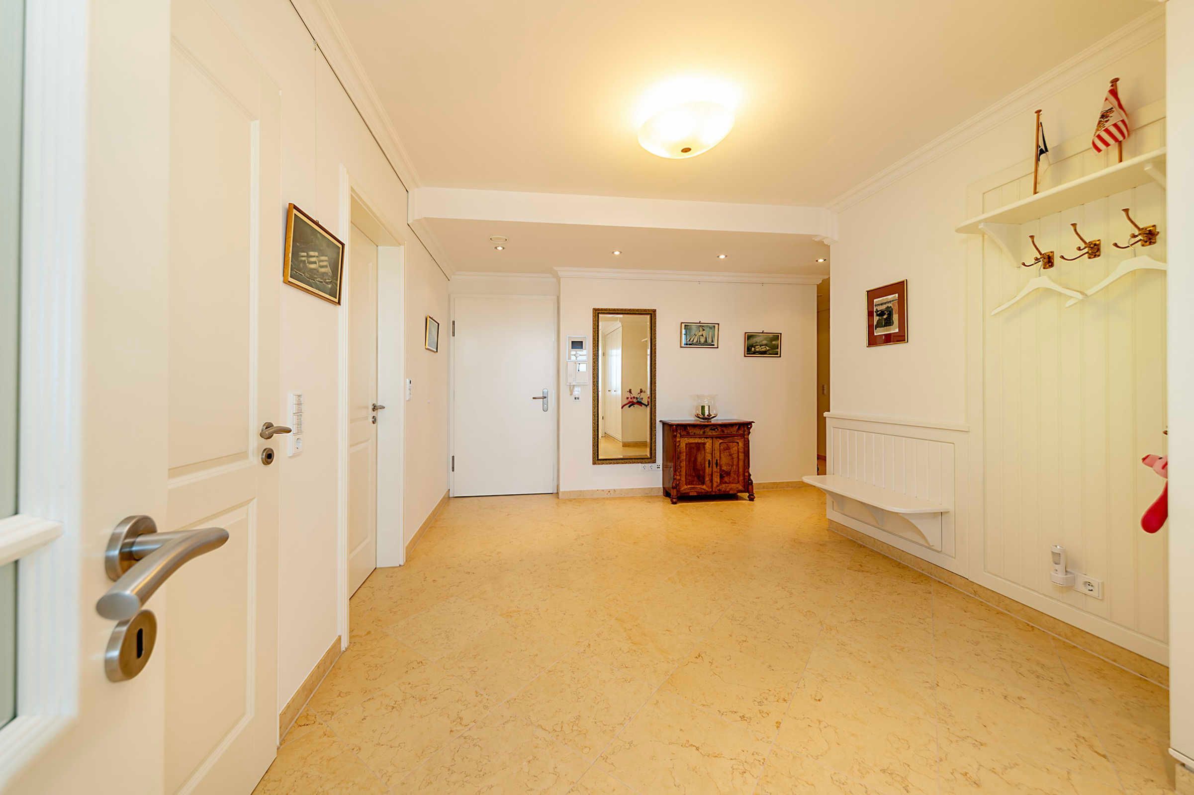 A hallway with white walls, a wooden cabinet, and a coat rack with hangers.