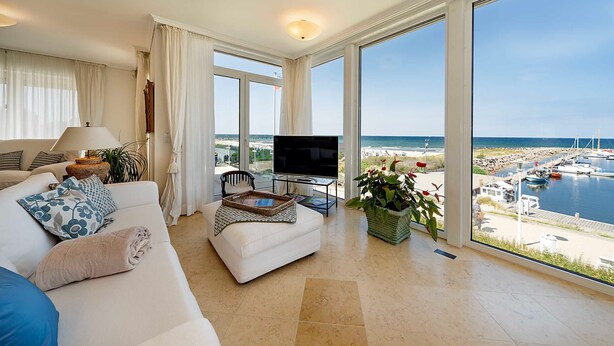 Ein modernes Wohnzimmer mit einer Couch, einem Fernseher und großen Fenstern mit Blick auf eine Marina.