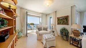 Ein Wohnzimmer mit Sofa, Hocker, Lampe, Bücherregal und einem Gemälde.