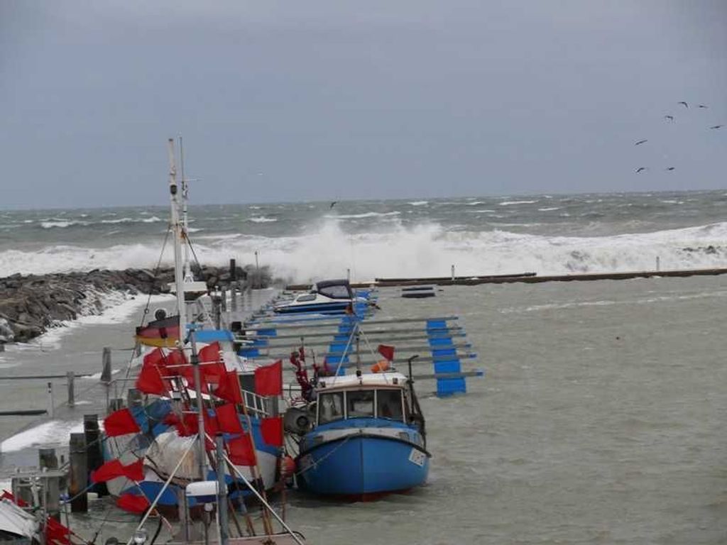 Ein Hafen mit vertäuten Booten, einer felsigen Küstenlinie und rauem Seegang.