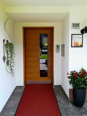 A hallway with a red carpet leading to a wooden door, a potted plant on the right, and a wall-mounted sign with the number 335. - Ritter Anna - Haus Panorama - Ferienwohnung (Schoppernau)