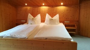 A wooden room with a bed, two pillows, a nightstand, and a wooden bench. - Ritter Anna - Haus Panorama - Ferienwohnung (Schoppernau)