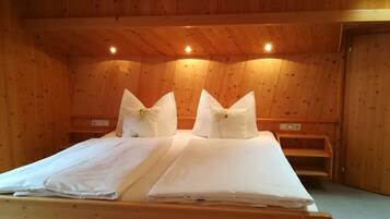 A wooden room with a bed, two pillows, a nightstand, and a wooden bench.