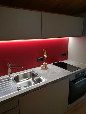A modern kitchen with a stainless steel sink, a built-in stove, and a red backsplash. - Ritter Anna - Haus Panorama - Ferienwohnung (Schoppernau)