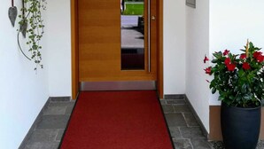 A hallway with a red carpet leading to a wooden door, a potted plant on the right, and a wall-mounted sign with the number 335. - Ritter Anna - Haus Panorama - Ferienwohnung (Schoppernau)