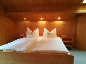 A wooden room with a bed, two pillows, a nightstand, and a wooden bench. - Ritter Anna - Haus Panorama - Ferienwohnung (Schoppernau)