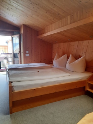 A wooden cabin with a large bed, a small table, and a door leading outside. - Ritter Anna - Haus Panorama - Ferienwohnung (Schoppernau)
