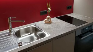 A modern kitchen with a stainless steel sink, a built-in stove, and a red backsplash. - Ritter Anna - Haus Panorama - Ferienwohnung (Schoppernau)