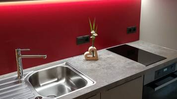 A modern kitchen with a stainless steel sink, a built-in stove, and a red backsplash.