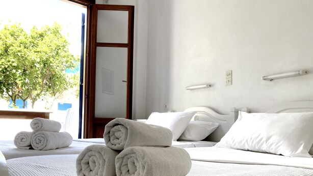 A hotel room with a neatly made bed, a bedside table, and a view of a tree outside. - Helliniko Studios - Adults Only  (Paros)