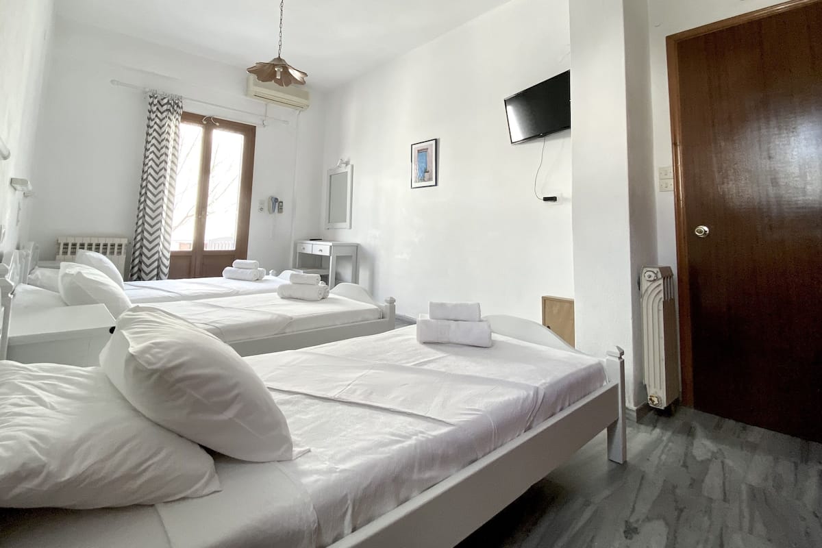 A hotel room with two beds, a TV, a mirror, a window with curtains, and a radiator.