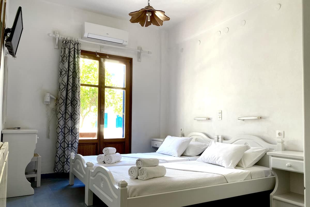 A clean, white bedroom with a bed, bedside tables, and an air conditioning unit.