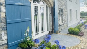 A stone building with a large arched entrance, a blue door, and a small garden with blue flowers. - The Granary, 18th Century Luxuriously Restored Barn in the Heart of Tipperary (Thurles)