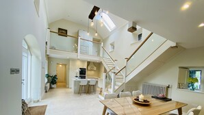 A spacious kitchen with a central island, a dining area with a wooden table and white chairs, and a staircase leading to an upper level. - The Granary, 18th Century Luxuriously Restored Barn in the Heart of Tipperary (Thurles)