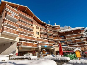 Un hotel de varios pisos con balcones, un cartel de alquiler de esquíes y un restaurante llamado 'Le Barillon' en un paisaje nevado.