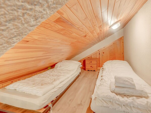Um quarto de sótão pequeno com duas camas de solteiro, paredes de madeira e teto inclinado.