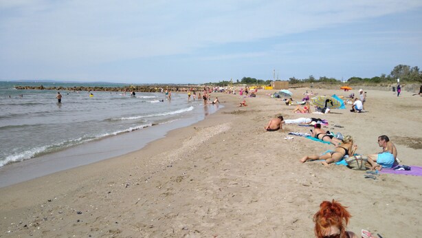 Une plage bondée où les gens se prélassent au soleil et se baignent.