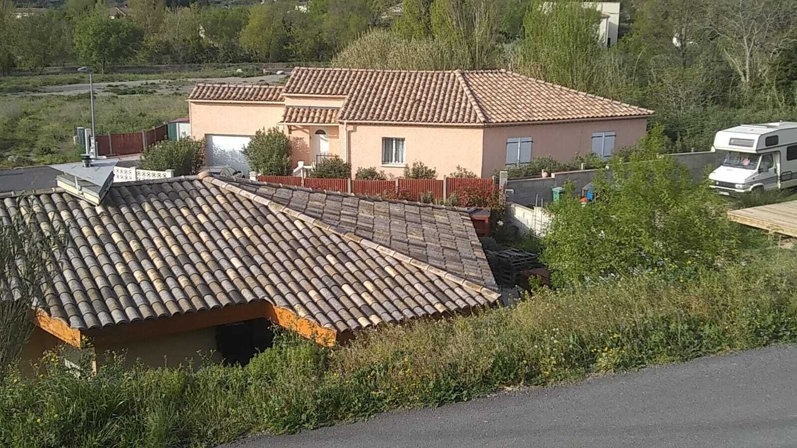 A residential building with a tiled roof, a fenced yard, and a parked camper.