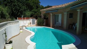 Une piscine à bordures courbes, entourée d’un mur blanc et d’une terrasse carrelée.