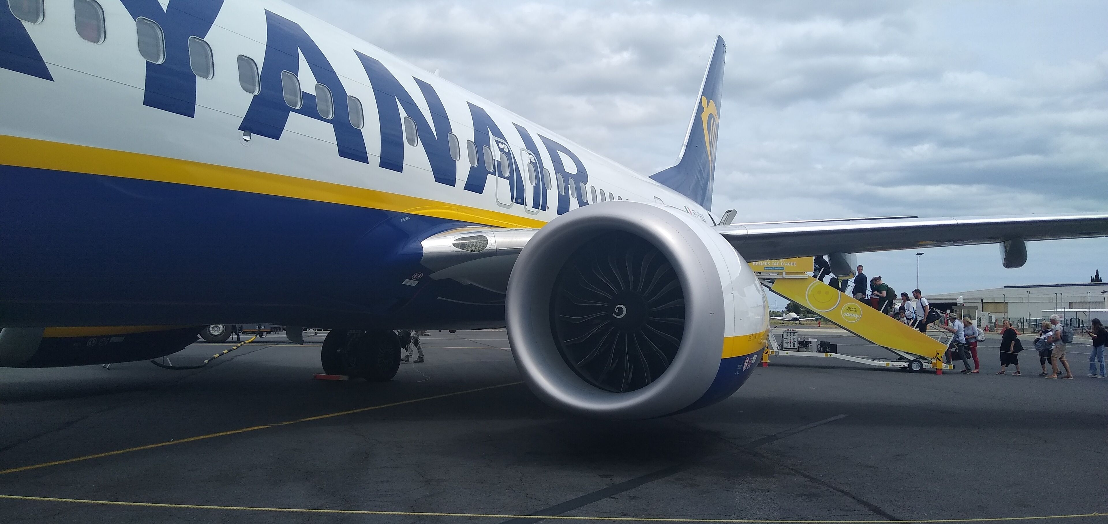An airplane with "YANAI AIRWAYS" written on its side, parked on the tarmac with passengers boarding via a jet bridge.