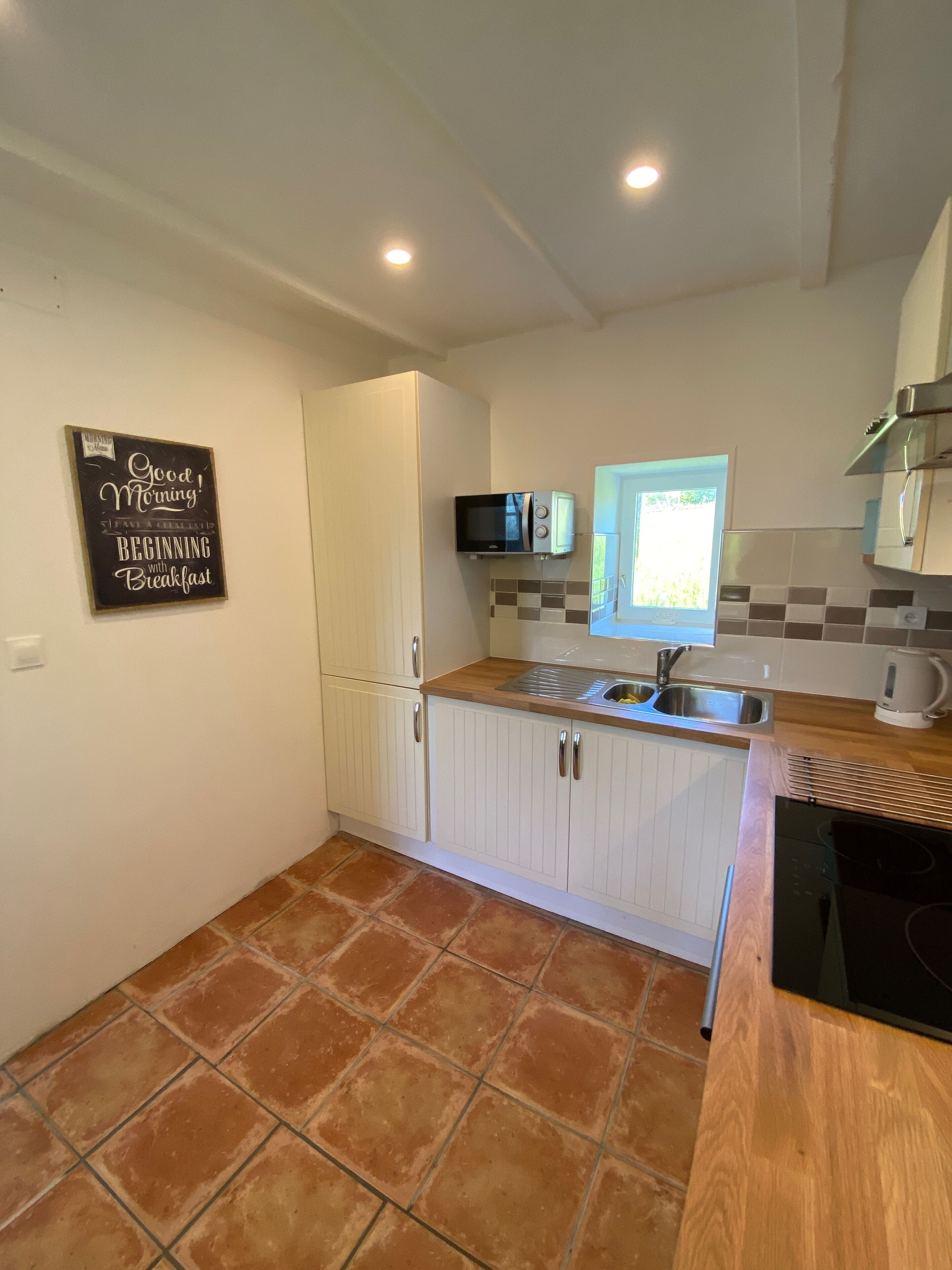 A compact kitchen with white cabinets, a microwave, a sink, and a window.