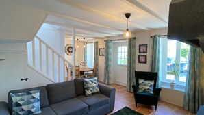 A living room with a grey sectional sofa, a patterned rug, a stone fireplace, and a staircase leading to an upper level. - Le Petit Maison - La Relierie (Gavray)