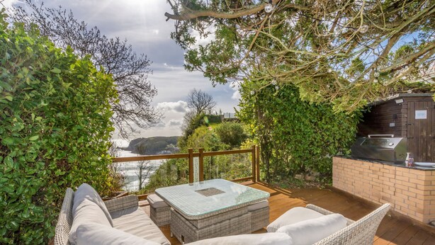 A wicker outdoor seating area with a glass-top table, a brick barbecue, and a view of the ocean.