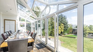 A modern dining room with a glass ceiling, large windows, and a view of a garden.