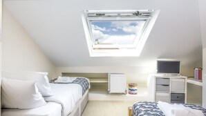 A bedroom with two beds, a skylight, a radiator, a TV, and a desk.