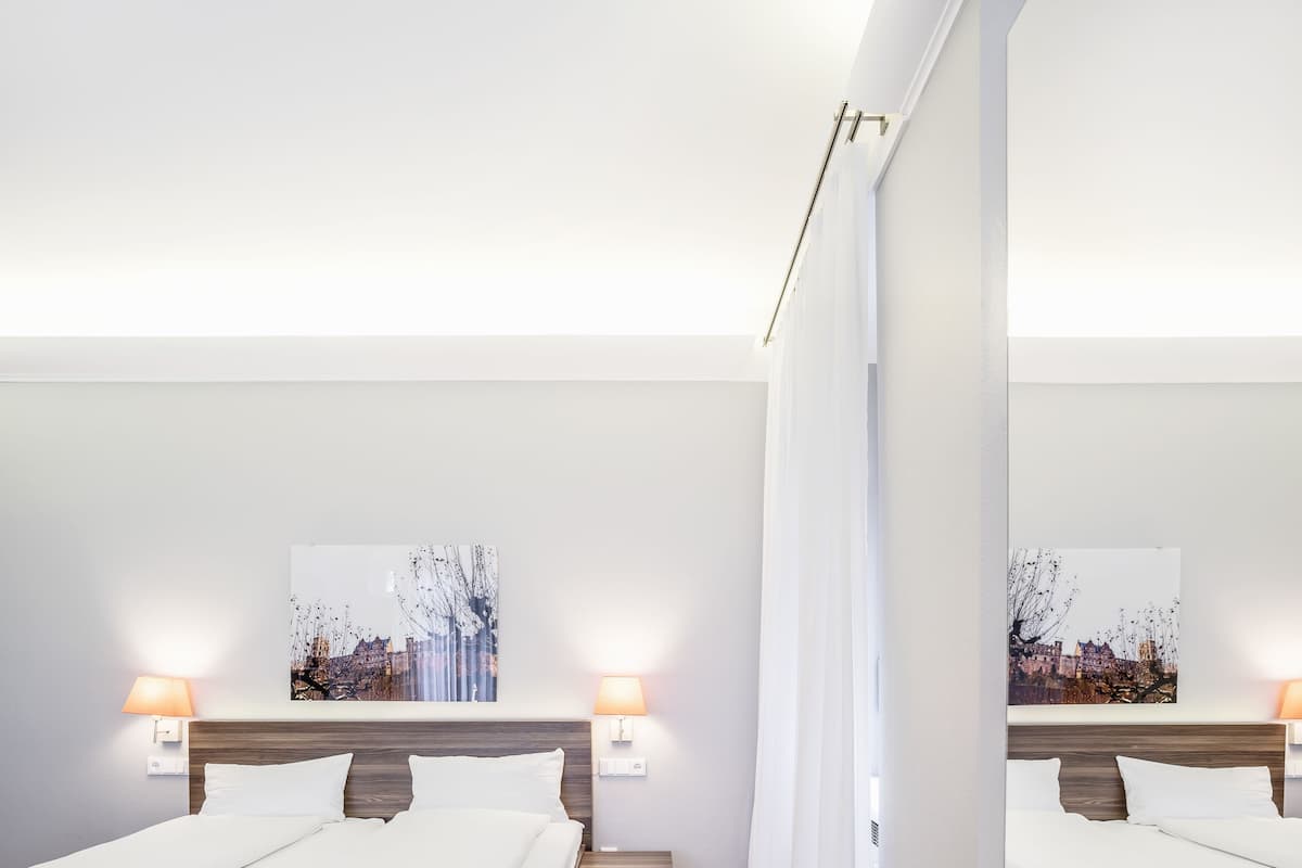 Une chambre d’hôtel moderne avec deux lits, un plancher en bois, des murs blancs et des œuvres d’art accrochées aux murs.
