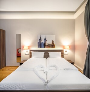 Habitación de hotel con una cama bien hecha, dos lámparas de noche, un cuadro de paisaje urbano en la pared y un cabecero de madera.