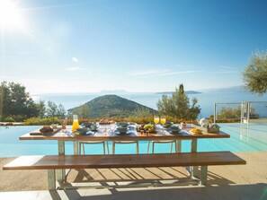 A dining table set with breakfast items and a view of a mountain and sea.
