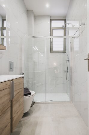 Un baño moderno con ducha envuelta en vidrio, inodoro y tocador con gabinete de madera.
