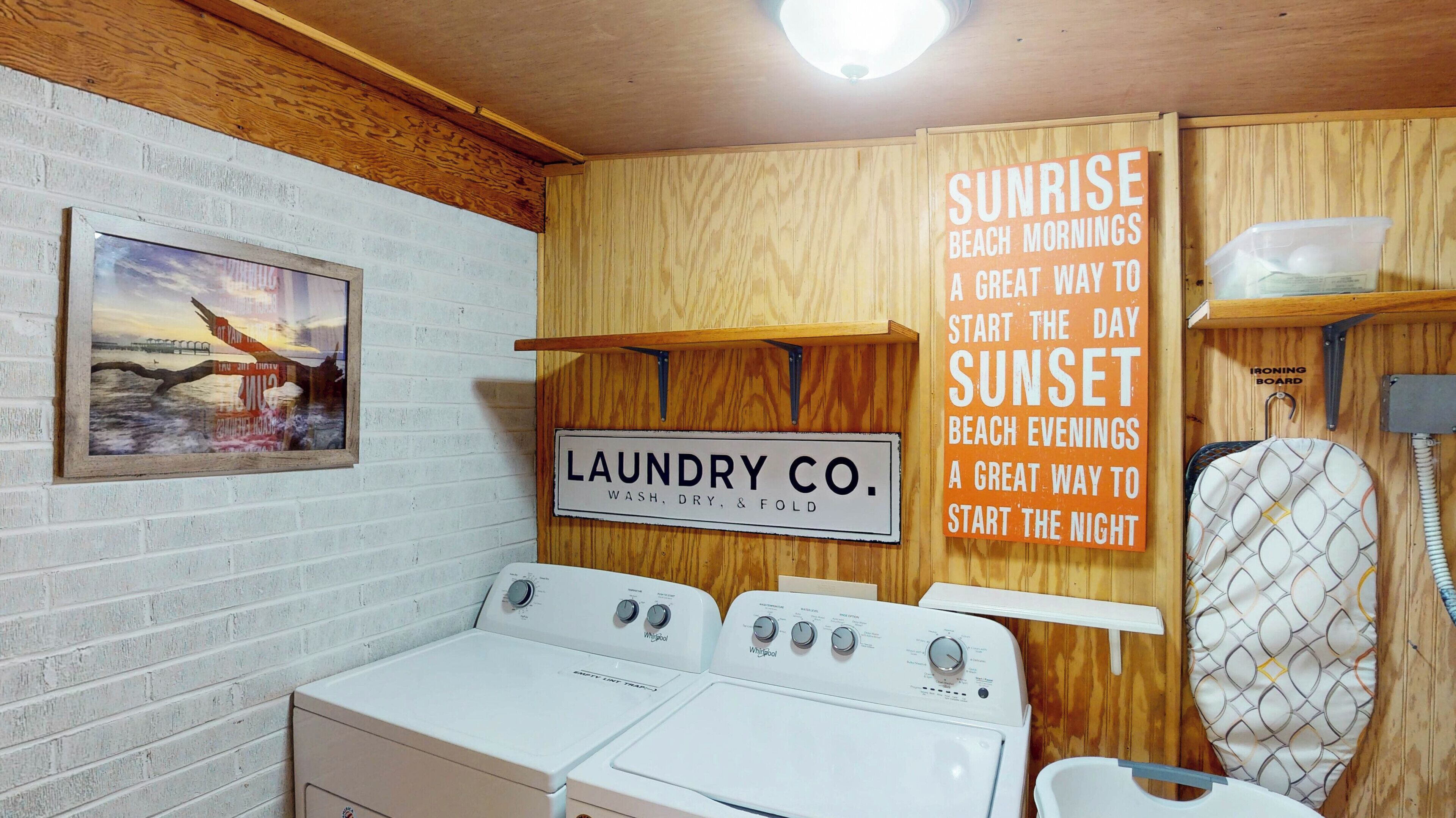 Une buanderie équipée de deux lave-linge Whirlpool, d’une enseigne indiquant « Laundry Co. » et d’une autre faisant la promotion des matinées et soirées à la plage.