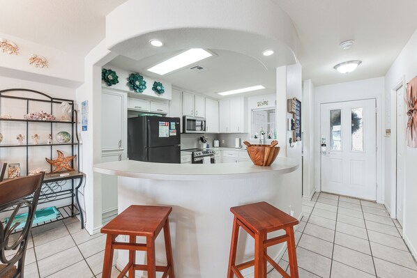 A kitchen with white cabinets, a black refrigerator, a microwave, and a sink. There are two wooden stools and a decorative starfish on a shelf.