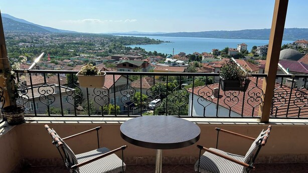 Un balcón con una mesa y dos sillas, con vista a un paisaje pintoresco de un lago y edificios circundantes.
