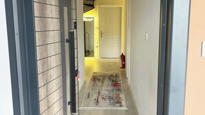 Un pasillo con pared de paneles de madera, una puerta blanca, un tapete pequeño y un extintor.