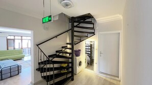 Un interior moderno con una escalera espiral negra, un área de lavandería a la vista y una señal de salida verde.